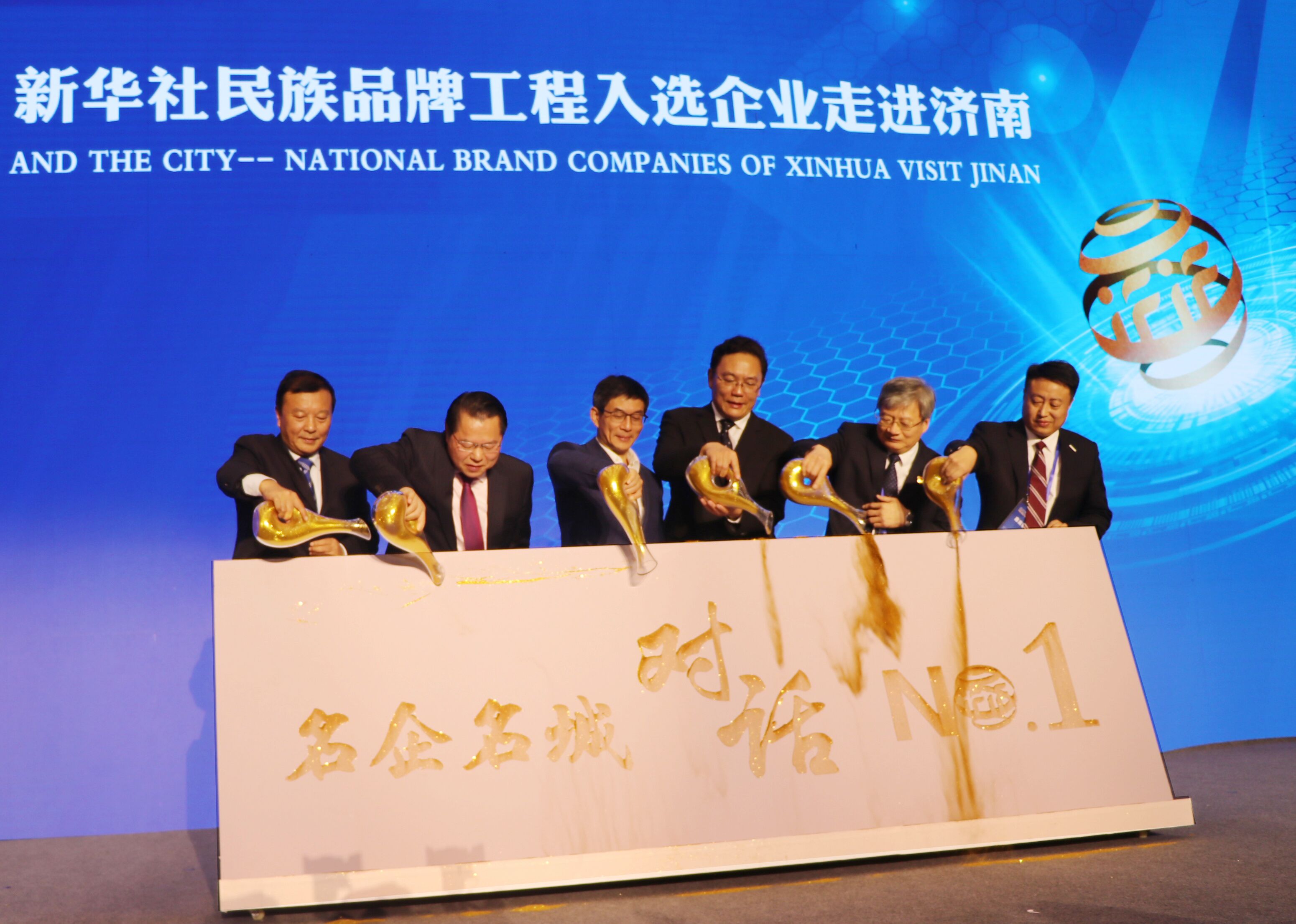 圖為新華通訊社副社長(cháng)兼秘書(shū)長(cháng)劉正榮（左三），濟南市委常委、副市長(cháng)，徐群（右三），全國政協(xié)委員、月星集團董事局主席丁佐宏（左二），全國人大代表，江蘇今世緣酒業(yè)董事長(cháng)、總經(jīng)理周素明（左一），中國重汽集團副總裁宋其東（右二），浪潮集團副總裁盧文杰（右一）共同“澆金”，啟動(dòng)首期名企名城對話(huà)——新華社民族品牌工程入選企業(yè)走進(jìn)濟南儀式。